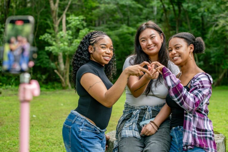 Three smiling friends making heart shape with hands.